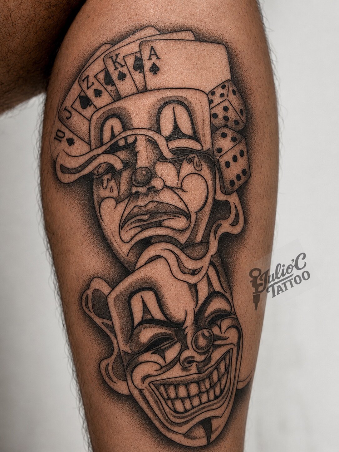 Tatuaje black and grey de naipes y rostros de arlequín en el brazo